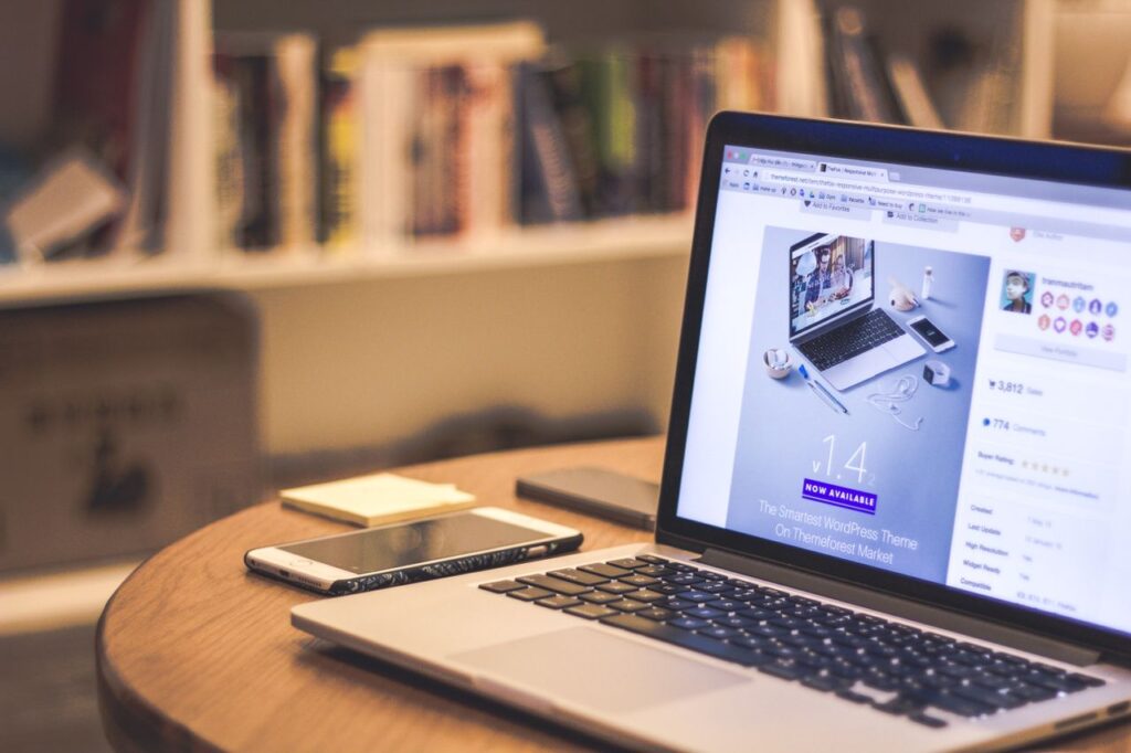 pexels photo 69432 A cozy modern workspace featuring a laptop displaying a website, a smartphone, and books on shelves.